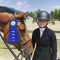 Rider standing with her horse and blue ribbon